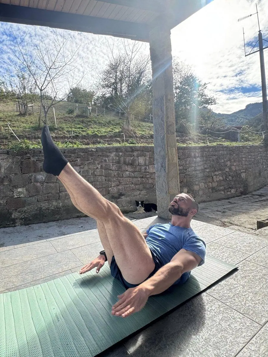 Antonio Jamart haciendo un ejercicio de Pilates sobre una esterilla en una terraza con vistas al monte